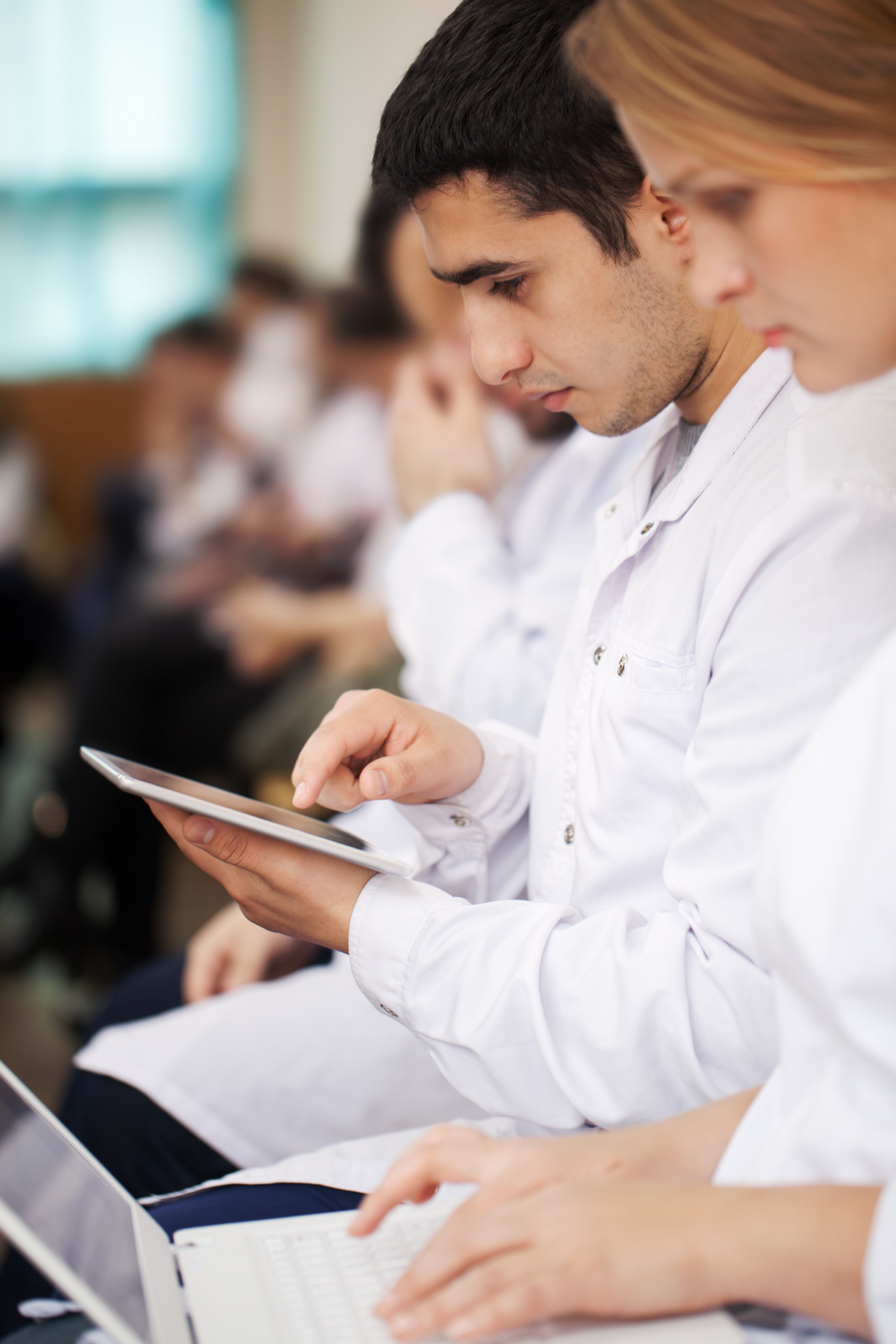 Modern medical students or doctors in auditorium during lecture or conference. They taking notes using laptop and tablet computer